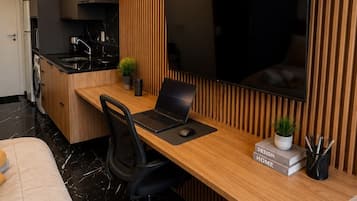 Una cocina moderna con estufa integrada, una zona de comedor con mesa de madera y sillas negras, y un televisor de pantalla plana grande montado en la pared.