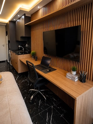 A modern kitchen with a built-in stove, a dining area with a wooden table and black chairs, and a large flat-screen TV mounted on the wall. - Ibirapuera Luxuoso studio Premium,cowork (São Paulo)