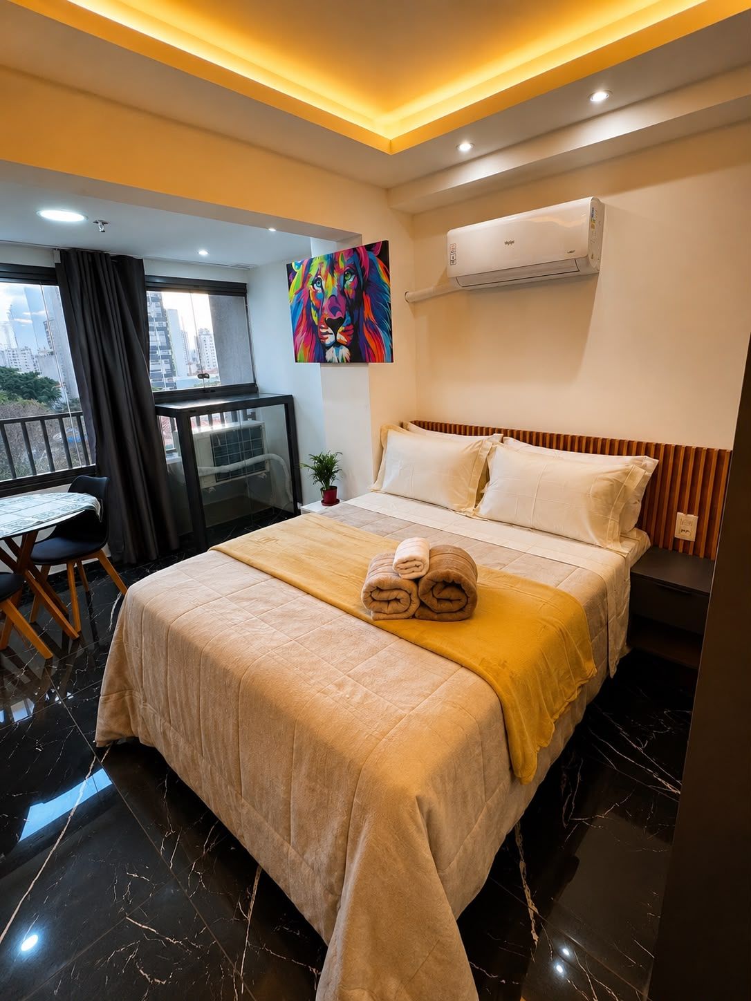 A hotel room with a bed, a desk, and a view of the city.