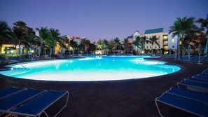 Una gran piscina envoltada de gandules i palmeres, amb edificis d'hotel al fons.