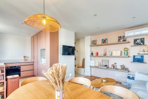 A modern kitchen with a dining area, featuring a round wooden table, chairs, a hanging light fixture, and a television mounted on the wall. - Le Minéral - Métro C - Caluire proche hôpital Croix Rousse - Climatisé (Caluire-et-Cuire)
