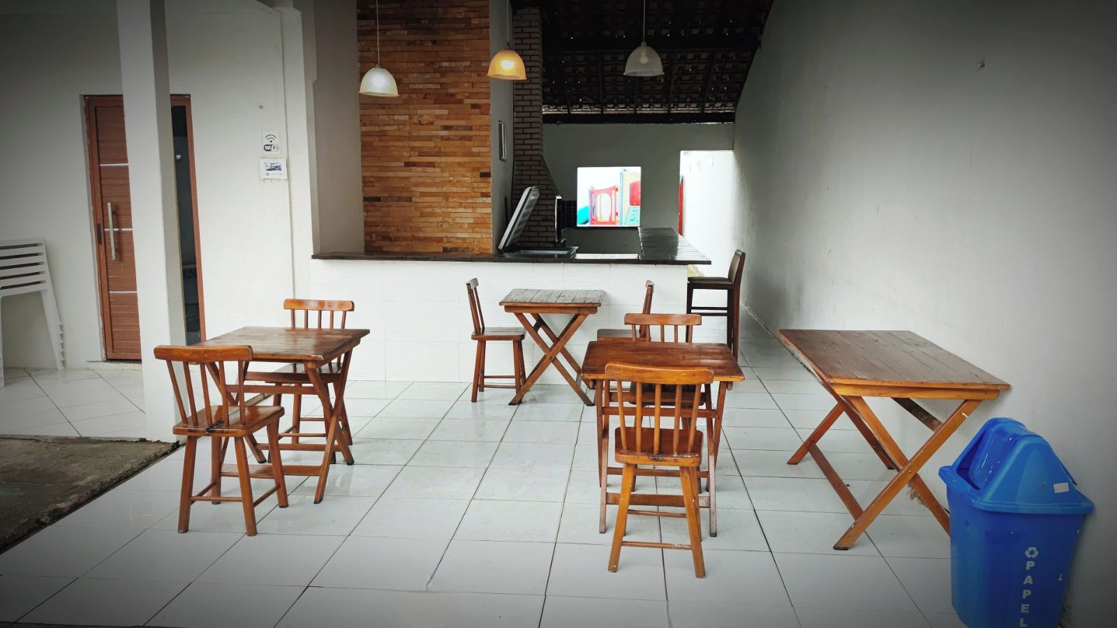 A dining area with wooden tables and chairs, a blue trash bin, and a staircase leading to an upper level.