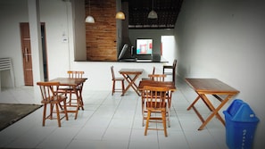 A dining area with wooden tables and chairs, a blue trash bin, and a staircase leading to an upper level. - Casa de Hospedagem Duplex Linda na Praia do Meio/Araçagy98.9.8.8.3.7-9.4.6.0 (São José de Ribamar)