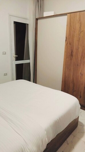 A bedroom with a bed, a wardrobe, and a door with curtains. - Family 2BR Mountain View La Prestigia (Hurghada)