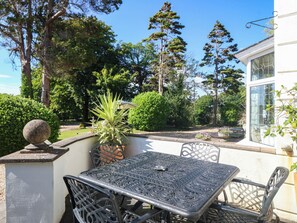 An outdoor patio with a metal table and chairs, surrounded by greenery and trees. - Meifod Country House (Caernarfon)