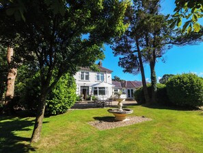 A two-story house with a well-maintained lawn and a central fountain. - Meifod Country House (Caernarfon)
