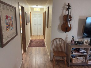 Ein Flur mit Holzboden, einem roten Teppich mit Muster, einem Holzstuhl, einer Violine und einem Fernseher auf einem Schrank.