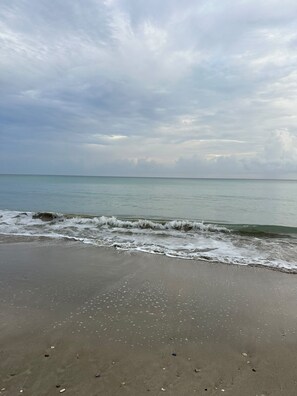A beach with waves gently lapping onto the shore under a cloudy sky.