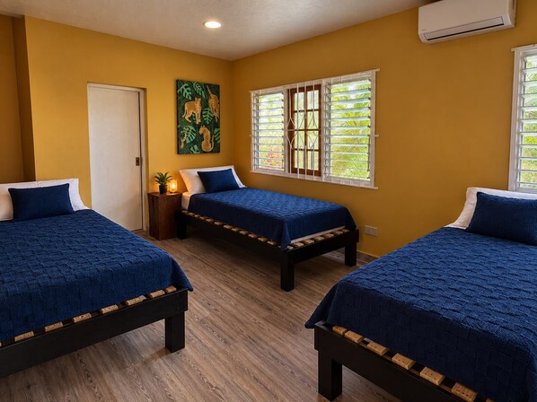 A room with three beds, a door, a window with blinds, and an air conditioning unit.