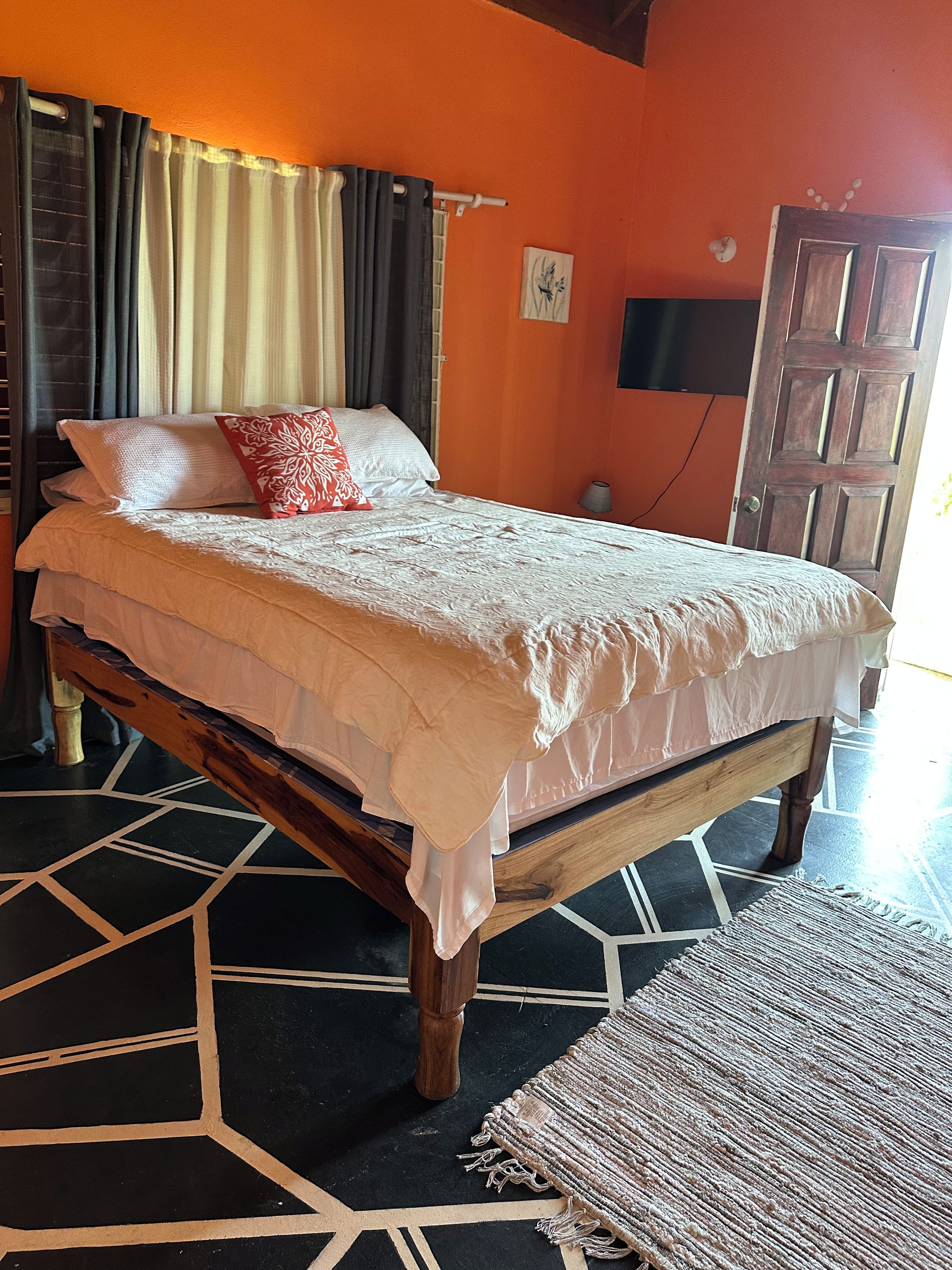 Ein Bett mit weißer Bettdecke und Kissen, ein Holz-Kopfbrett, ein gemustertes Parkett und eine Tür im Hintergrund.