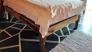 Ein Bett mit weißer Bettdecke und Kissen, ein Holz-Kopfbrett, ein gemustertes Parkett und eine Tür im Hintergrund.