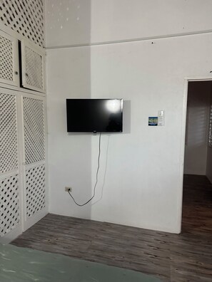 A room with a mounted flat-screen TV, a power outlet, and a thermostat on the wall.
