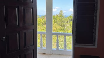 Une pièce dotée d’une grande porte en bois, d’un balcon avec une balustrade blanche et offrant une vue sur la verdure et le ciel.