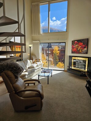 A spacious living room with a leather sofa, a glass coffee table, a fireplace, and a large window offering a view of a balcony and outside buildings. - SHE306 Fabulous 1 bedroom + loft by the Super Bee Lift, makes a vacation perfect (Frisco)