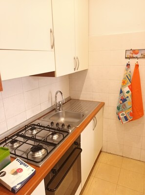 Una cocina con armarios blancos, un lavamanos de acero inoxidable y una estufa a gas.
