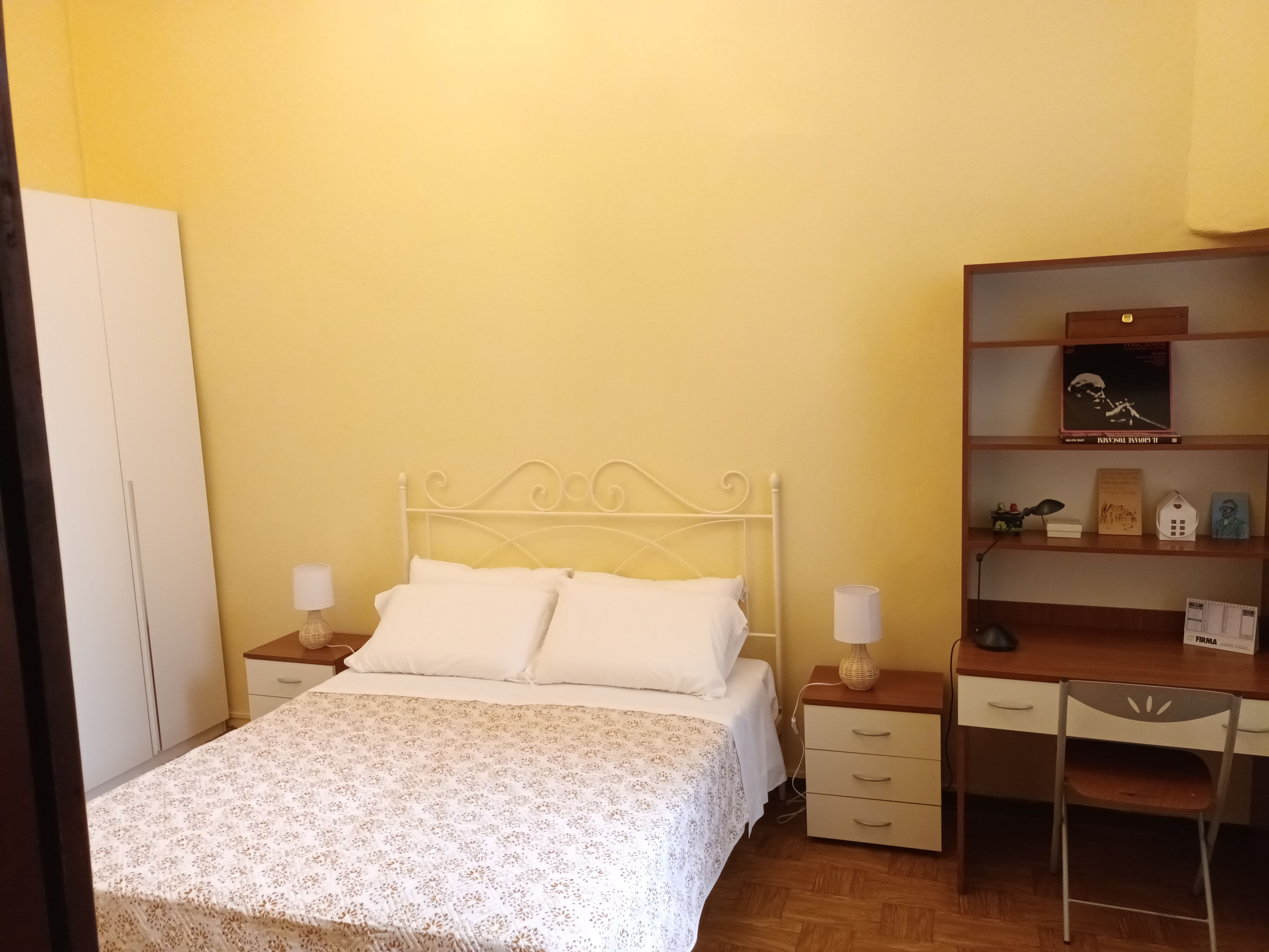 A bedroom with a bed, bedside tables, a desk, and a chair.