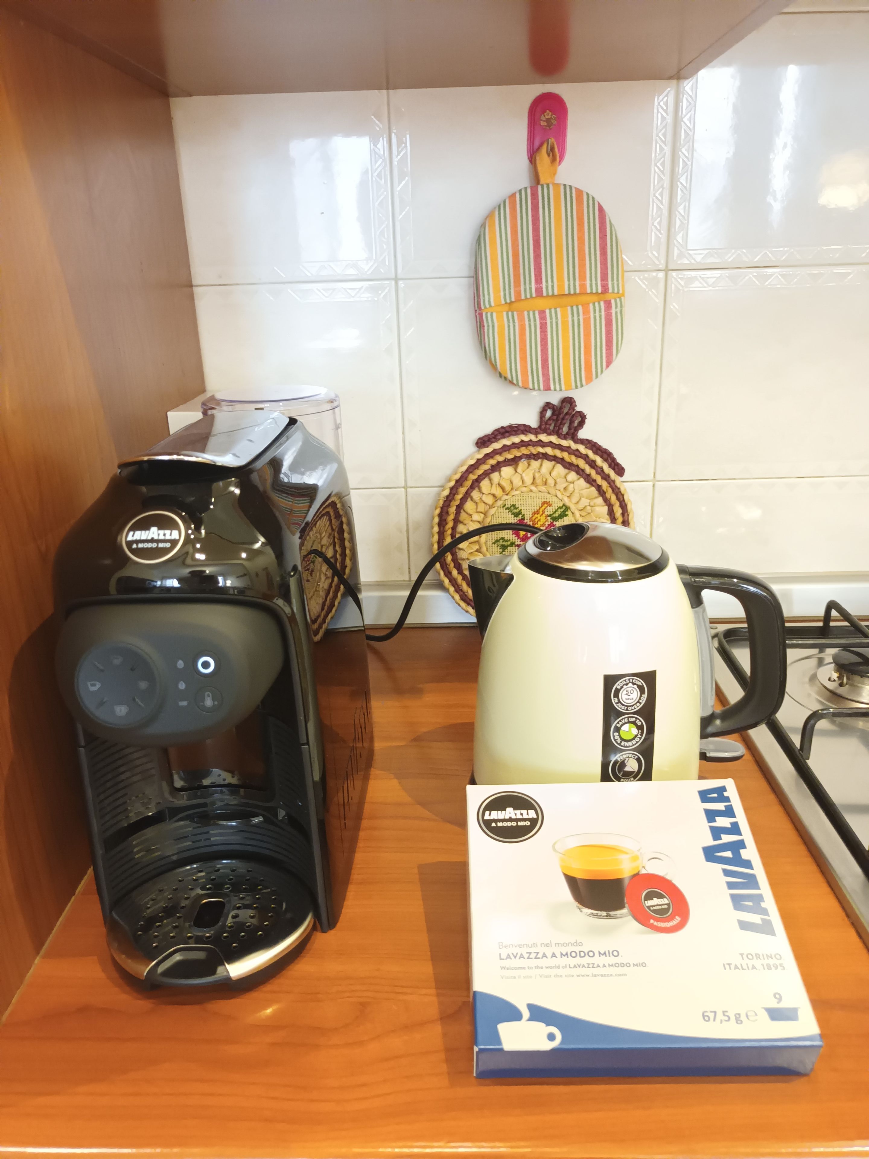 Eine Kaffeemaschine, ein Wasserkocher und eine Kapselbox stehen auf einer Küchenarbeitsplatte.