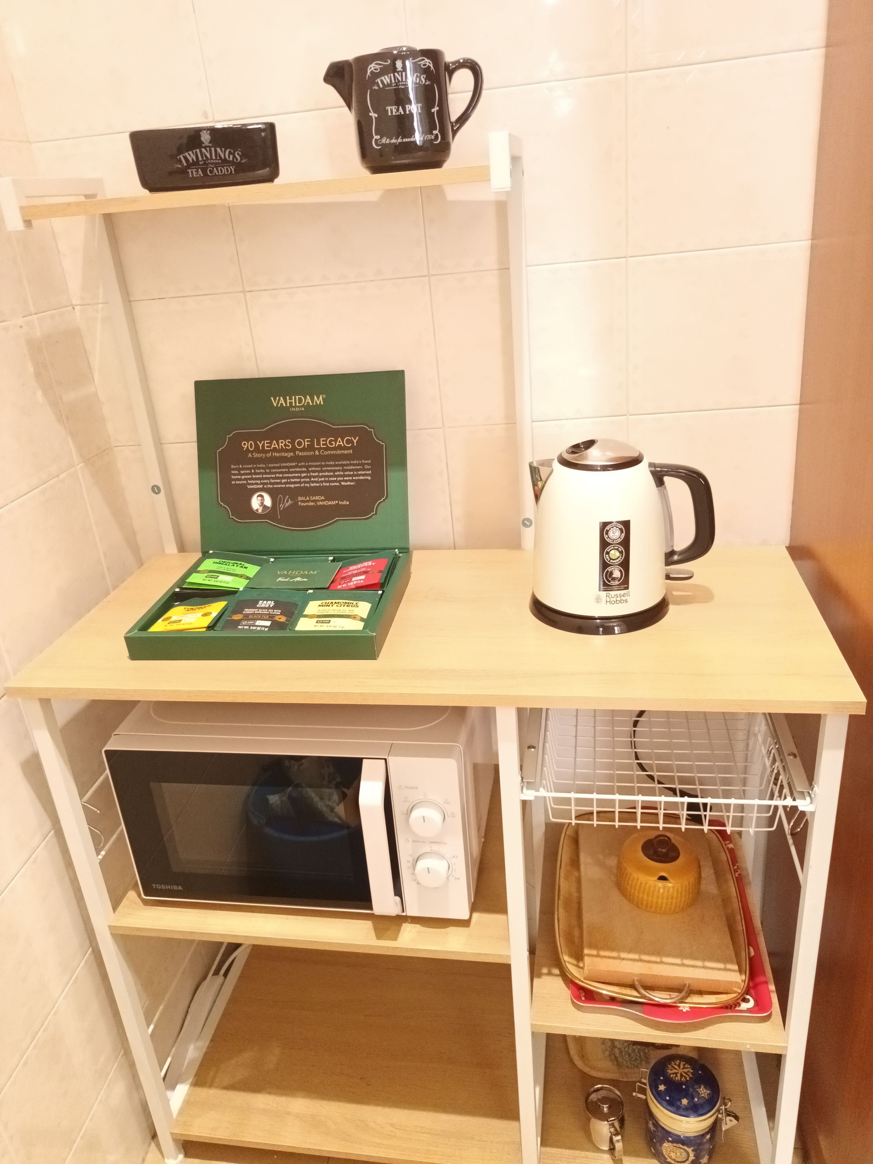 A kitchen area with a microwave, a kettle, a tea caddy, and a framed certificate on the counter.