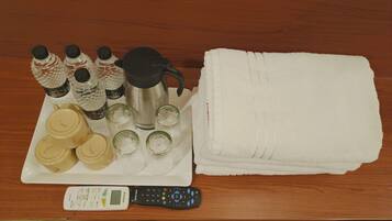 A table with a remote control, a white towel, a stainless steel water bottle, a black thermos, and several glass bottles with labels.