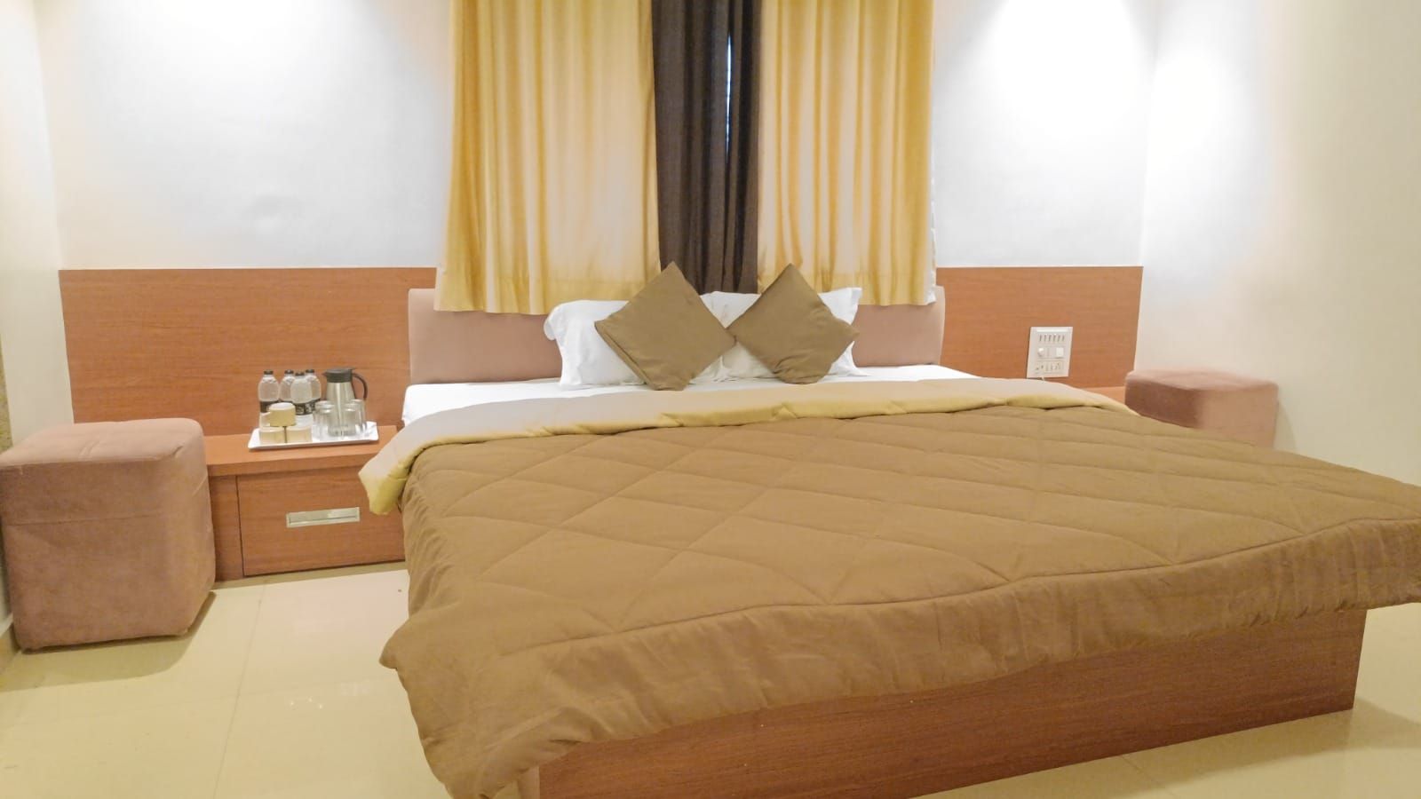 Una habitación de hotel con una cama grande, mesitas de noche y un ventanal con cortinas.