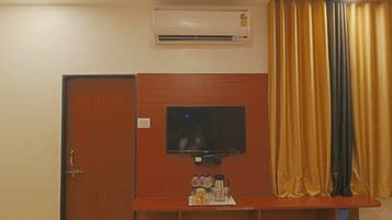 A room with a closed door, an air conditioning unit, a flat-screen TV mounted on a wooden panel, and a curtain.