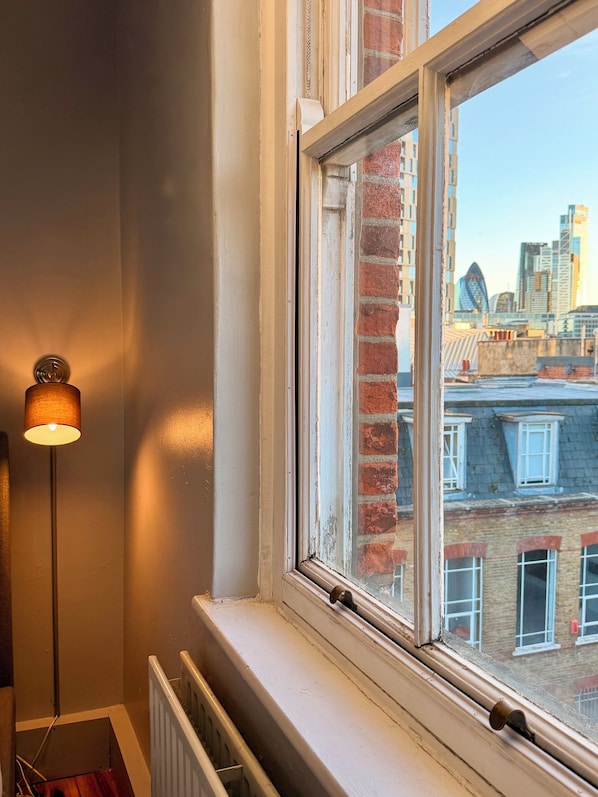 Ein Zimmer mit Fenster und Blick auf die Stadt, einem Heizkörper und einer Stehlampe.