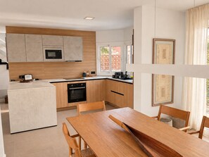 A modern kitchen with a central island, wooden cabinets, and a dining area with a wooden table and chairs. - Spherae Magma (Corralejo)