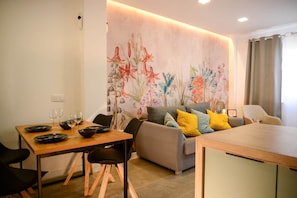 A dining area with a table set for two, a sofa, and a small kitchenette. - Spherae Nebula (El Cotillo)