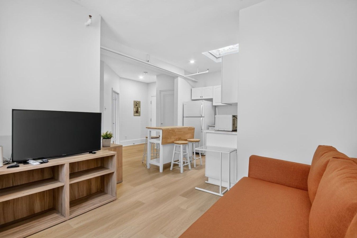 Un salon moderne avec un téléviseur à écran plat, un meuble de rangement en bois et un canapé orange.