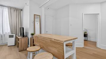 Una habitación moderna y minimalista con un escritorio de madera, dos taburetes, un televisor y una pequeña planta.