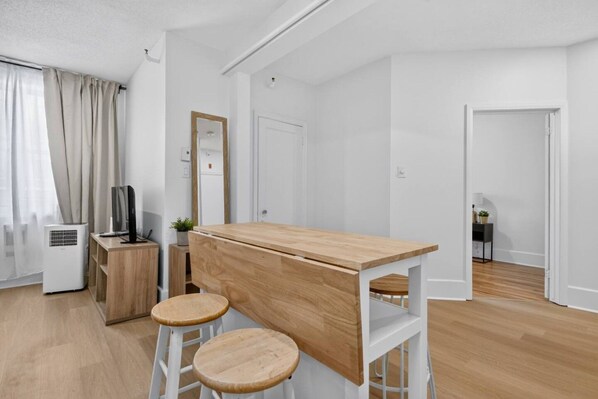 Habitació moderna i minimalista amb escriptori de fusta, dos tamborets, televisió i una petita planta.