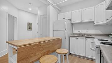 Een moderne keuken met witte kasten, een houten kookeiland met stoelen, een ingebouwde kookplaat en een koelkast.