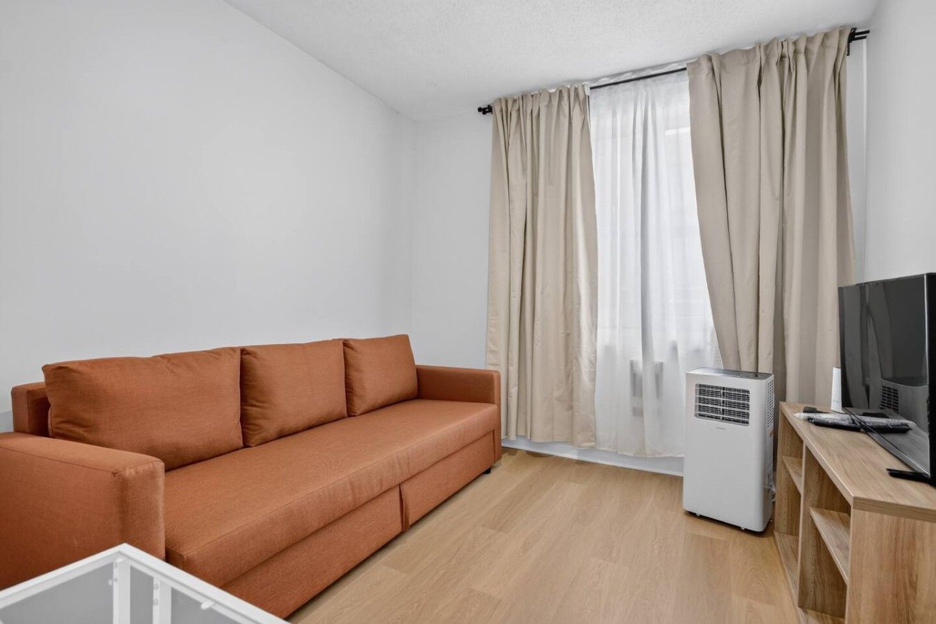Ett modernt vardagsrum med en soffa, en platt-TV och en vit luftkonditioneringsanläggning.