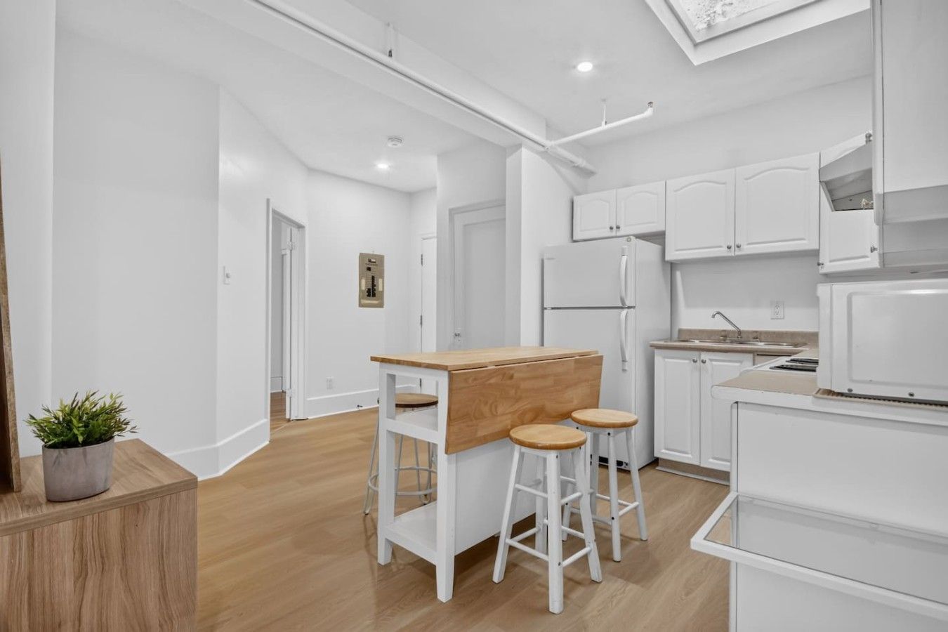 Une cuisine moderne avec des meubles blancs, un comptoir-bar en bois et deux tabourets.