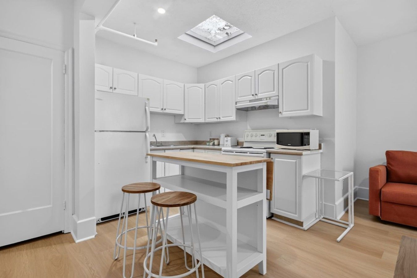 A modern kitchen with white cabinetry, a central island with stools, a microwave, and a stove.