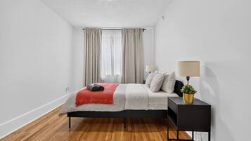 Ein modernes Schlafzimmer mit einem Bett, einem Nachttisch mit Lampe und einem Fenster mit Vorhängen.