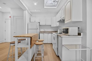 Eine kleine Küche mit weißen Schränken, einer Holz Arbeitsplatte und einer Mikrowelle. Es gibt Hocker und einen kleinen Tisch.