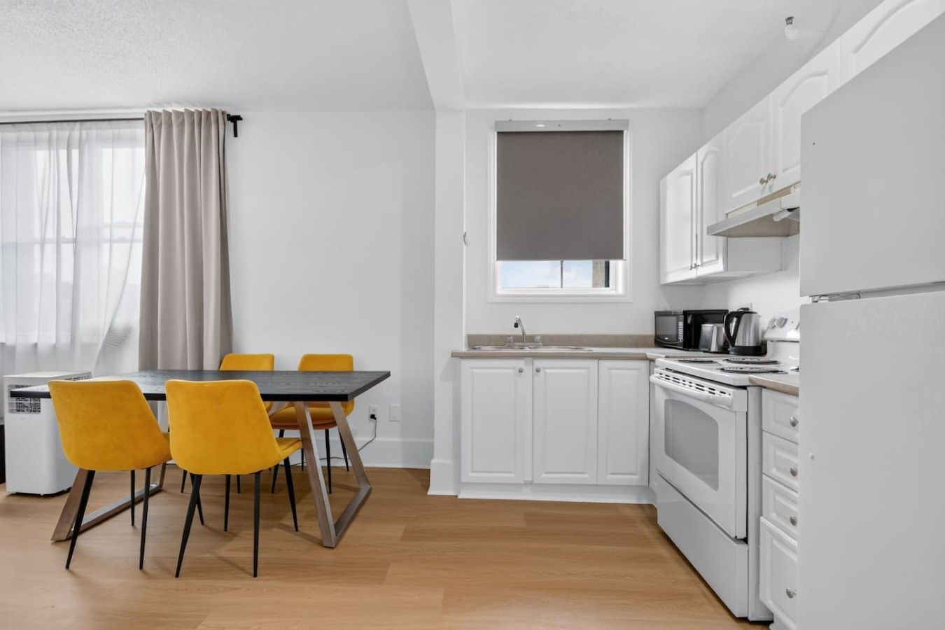 Een moderne keuken met witte kastjes, een zwart aanrecht en een eethoek met een tafel en gele stoelen.