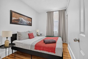 A bedroom with a bed, two bedside tables, a lamp, a painting, and a window with curtains. - The Modern Corner 1BR | Kitchen, A/C & Wi-Fi (Gatineau)