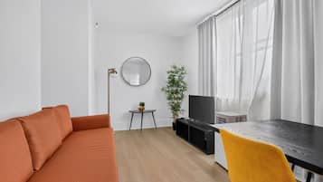 Una sala moderna con sofá, una mesa de comedor, televisor y una planta.