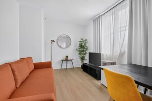 En moderne stue med sofa, spisebord, fjernsyn og en plante.