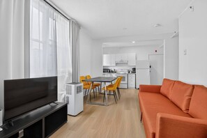 A modern living room with a flat-screen TV, a sofa, and a dining area with chairs. - The Modern Corner 1BR | Kitchen, A/C & Wi-Fi (Gatineau)