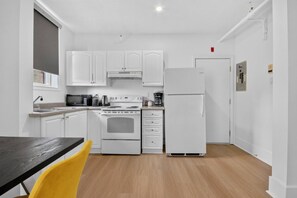 Una cocina compacta con armarios blancos, estufa, microondas y refrigerador.