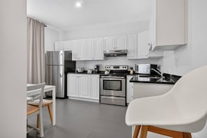 Een moderne keuken met witte kasten, roestvrijstalen apparatuur en een eethoek met een witte stoel.
