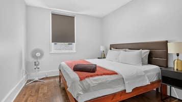 Ein Schlafzimmer mit einem Bett, Nachttischen, einem Fenster und einem Wandventilator.