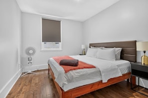 A bedroom with a bed, bedside tables, a window, and a wall-mounted fan. - Capital Region 1BR | Minutes to Attractions (Gatineau)