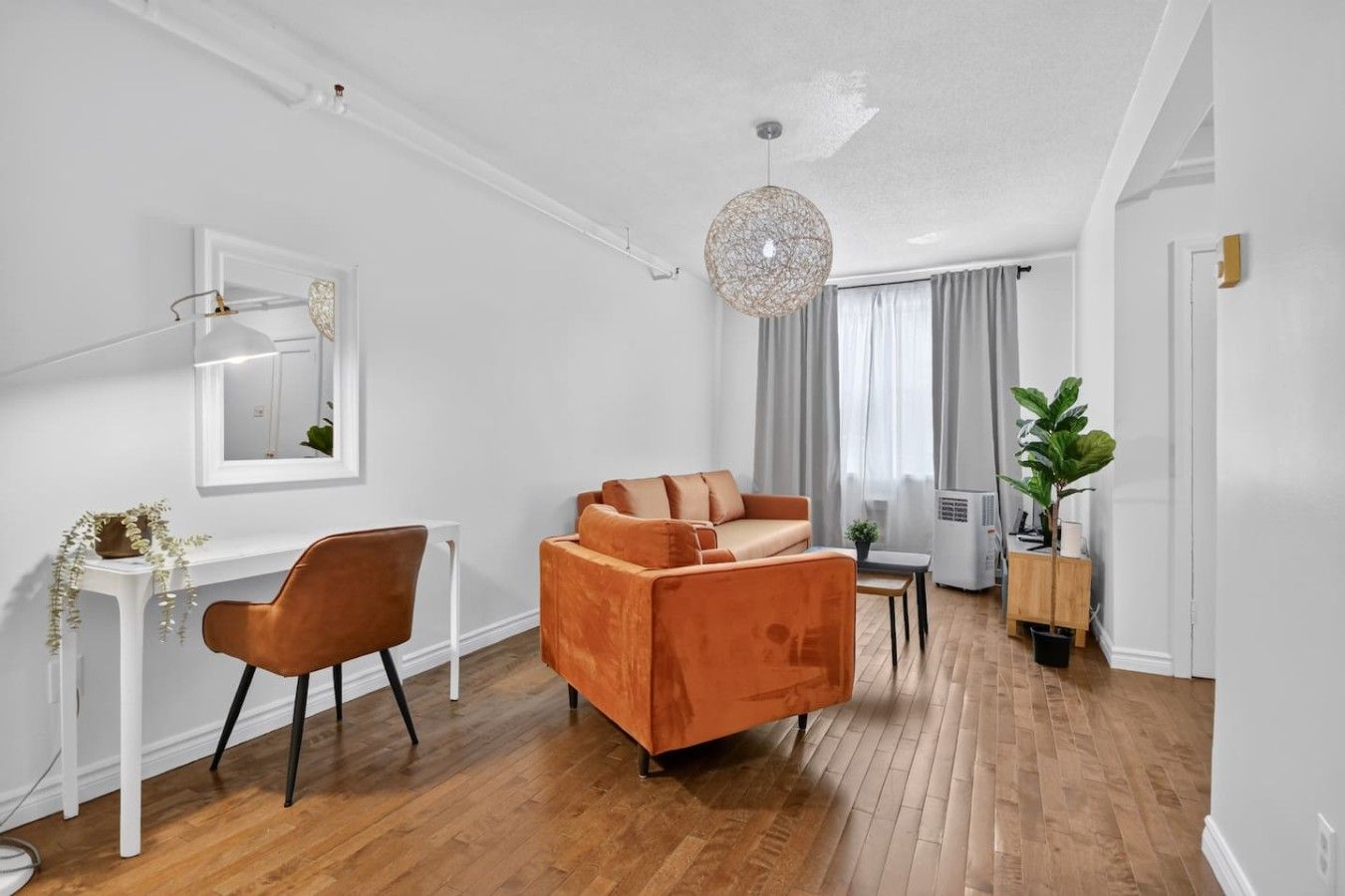A modern living room with a sofa, a chair, a small table, and a hanging light fixture.