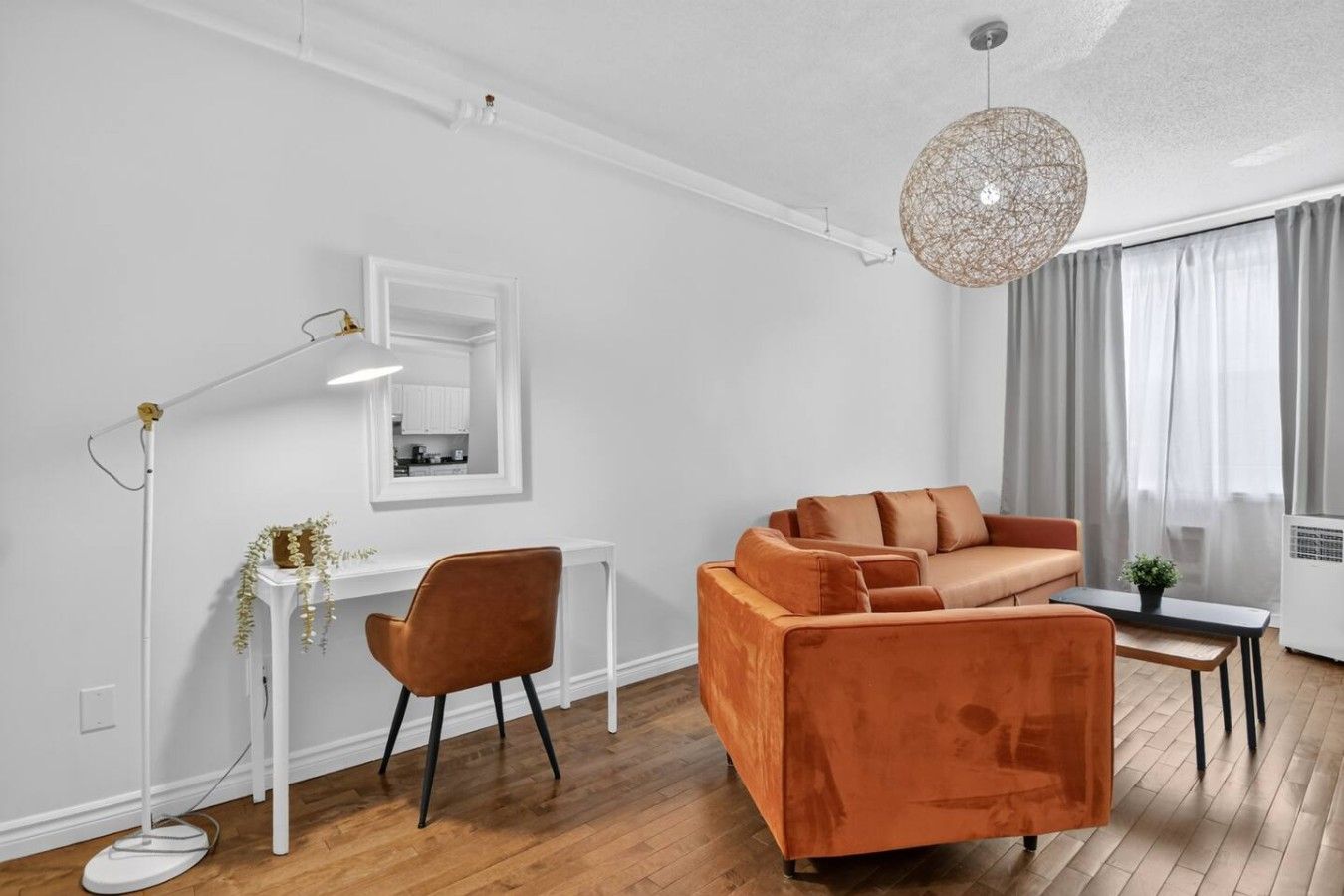En moderne stue med sofa, skrivebord, stol, gulvlampe og hængende lampe.