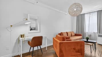 En moderne stue med sofa, skrivebord, stol, gulvlampe og hængende lampe.