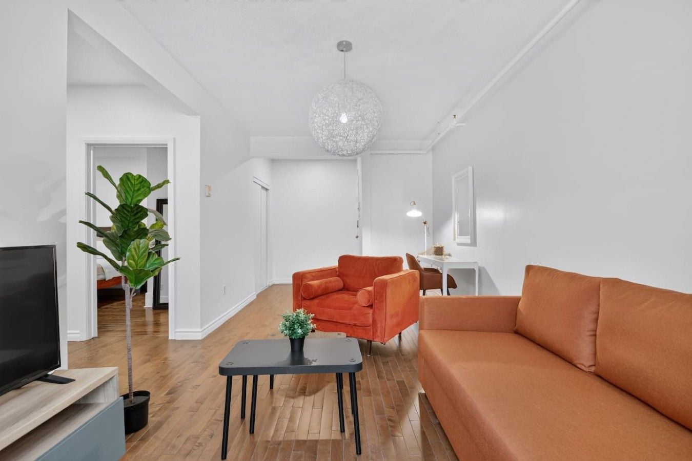 A modern living room with a sofa, armchair, and a TV on a stand.